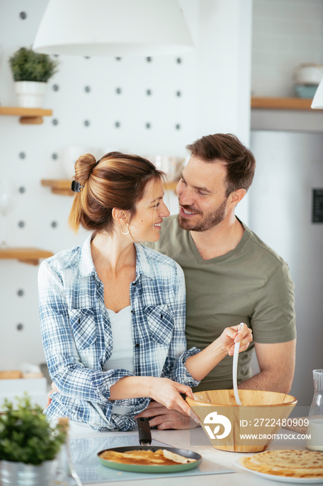 Young couple making pancakes at home. Loving couple having fun while cooking.