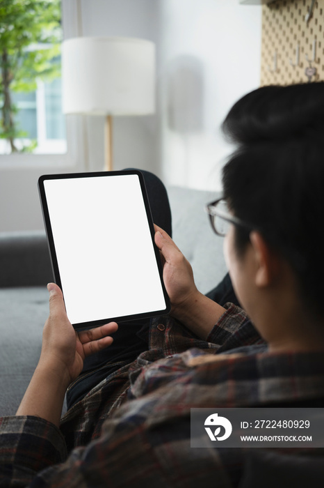 View over shoulder young man sitting on sofa and using digital tablet.