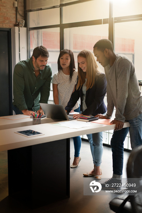 Four attractive co workers standing over desk going through presentation on computer