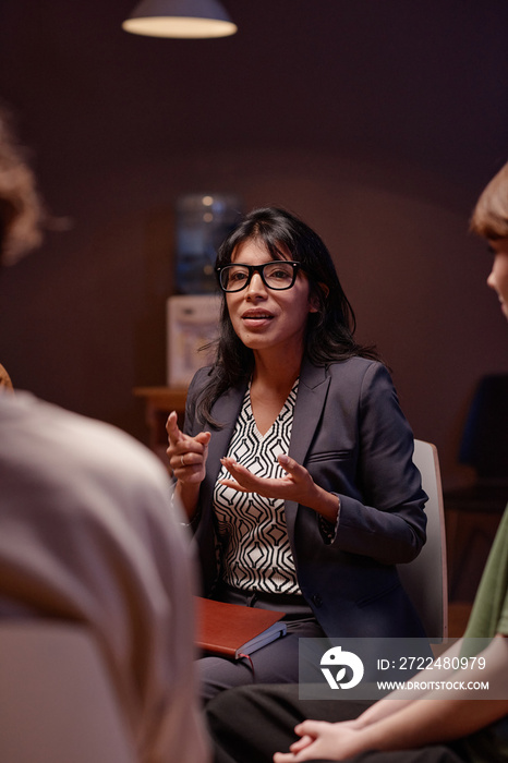 Vertical shot of modern psychotherapist working with group of people having depression discussing something with them