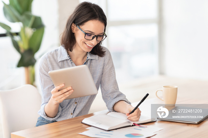 Girl writing in notebook and holding tablet