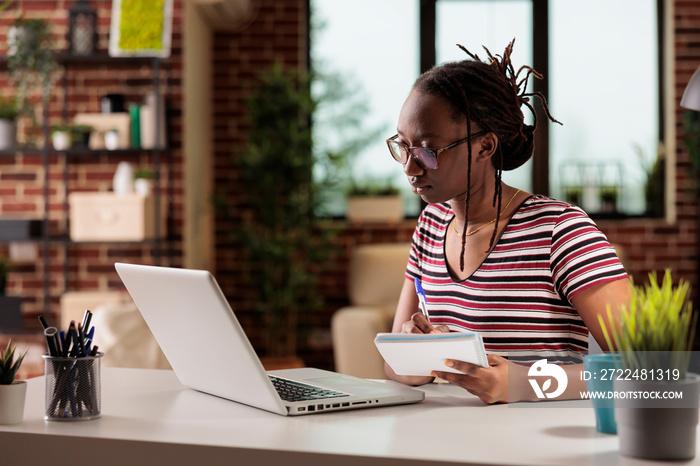 Student watching educational tutorial online on laptop, taking notes in notepad, doing homework. E learning, home education, distance university lesson, internet course classes