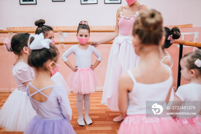 Group of beautiful little girls with protective face masks practicing ballet at dancing class. Coronavirus, Covid-19 concept.