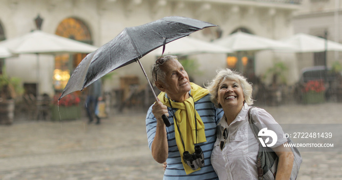 Happy senior tourists stand downtown and enjoy the rainy weather in Lviv