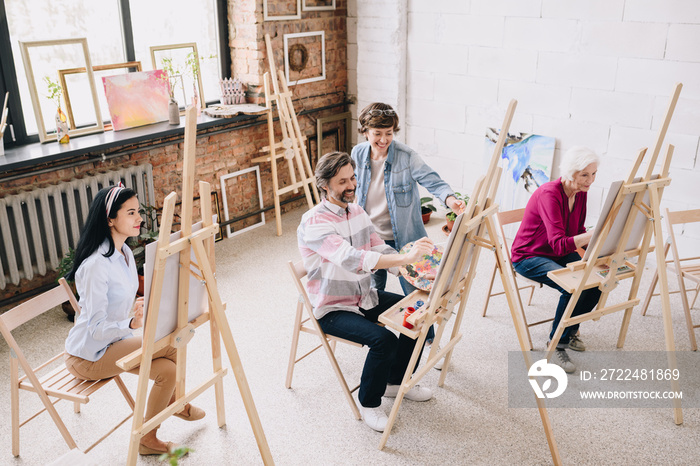 Wide angle portrait of female art teacher working with group of students painting at easels in spacious sunlit art studio, copy space