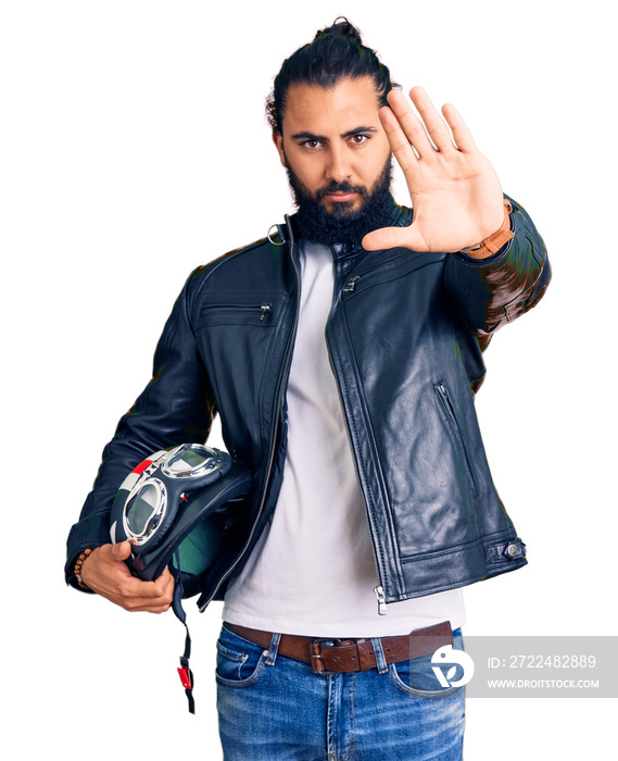 Young arab man holding motorcycle helmet with open hand doing stop sign with serious and confident expression, defense gesture