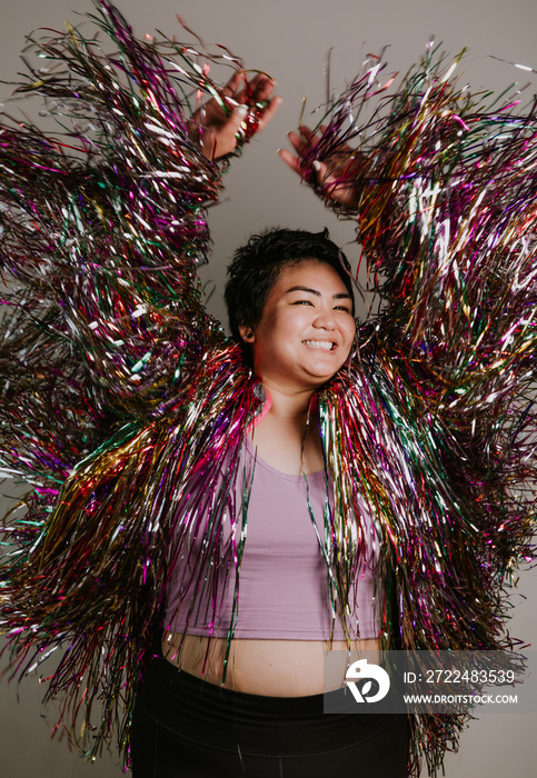 portrait of a plus size filipino woman wearing tinsel jacket arms up