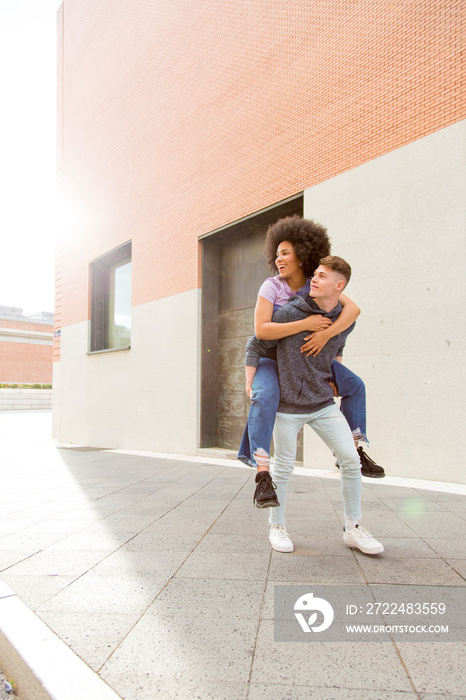 Caucasian young man carrying afro woman on his back on a sunny day