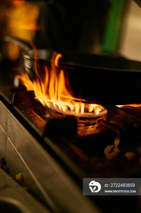 flame in the pan. Professional Chef makes flambe for food in the restaurant kitchen. Chef cooking with open fire pan.  on a stove. Fire burn is cooking on iron pan,stir fire very hot