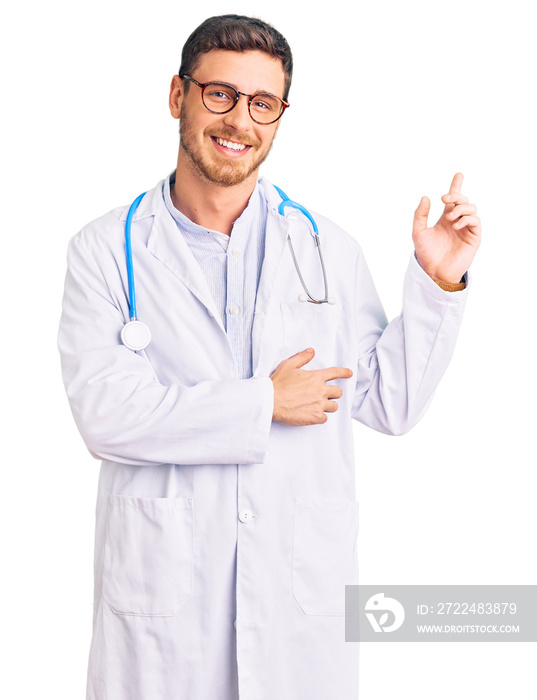 Handsome young man with bear wearing doctor uniform with a big smile on face, pointing with hand and finger to the side looking at the camera.