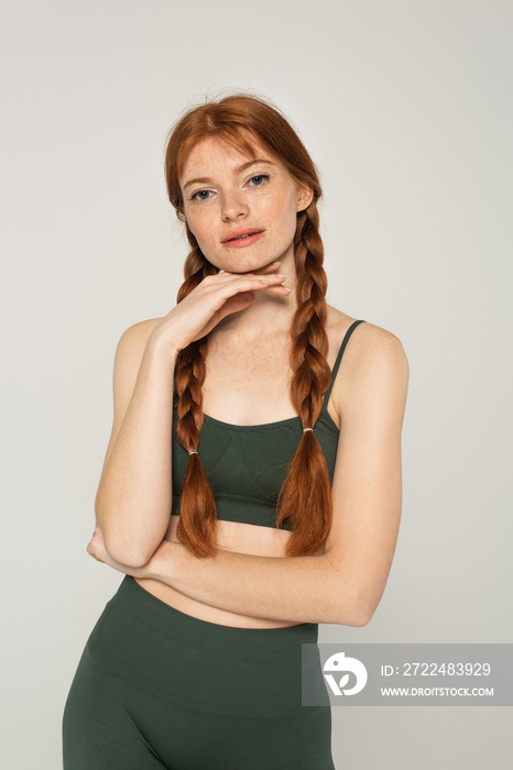 Redhead sportswoman with freckles looking at camera isolated on grey