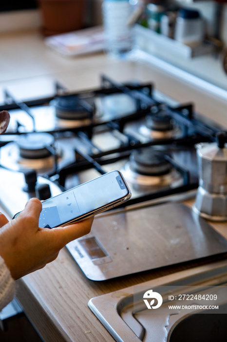 Mani di ragazza che controllano un o smartphone mentre in cucina  si prepara il caffè nello moka sullo sfondo