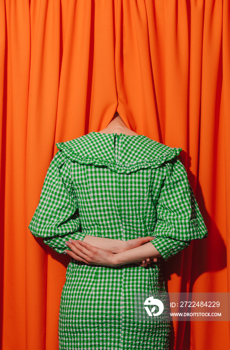 girl in a green dress hides her head in orange curtains