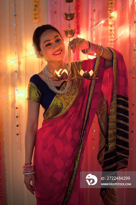 Beautiful Indian woman smiling while holding hanging diya lamps - Diwali Festival. Beautiful Indian woman smiling while holding diya oil lamps on diwali festival