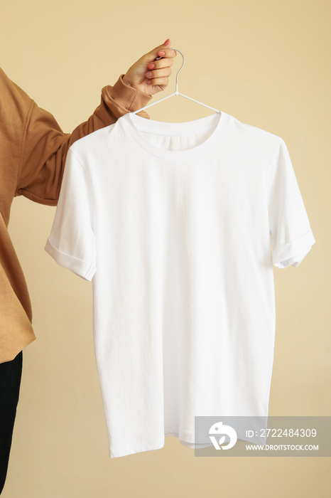 Woman hold hanger with blank white t-shirt on beige background