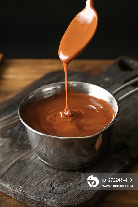 Liquid caramel pouring from spoon into pot on table