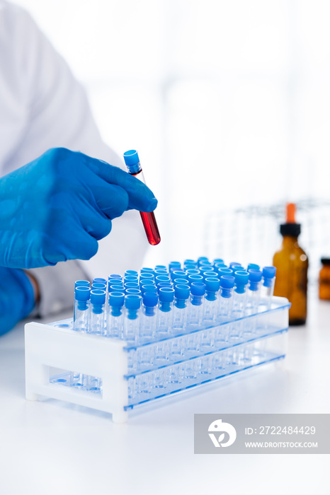 Lab assistant, a medical scientist, a chemistry researcher holds a glass tube through the blood sample, does a chemical experiment and examines a patient’s blood sample. Medicine and research concept.