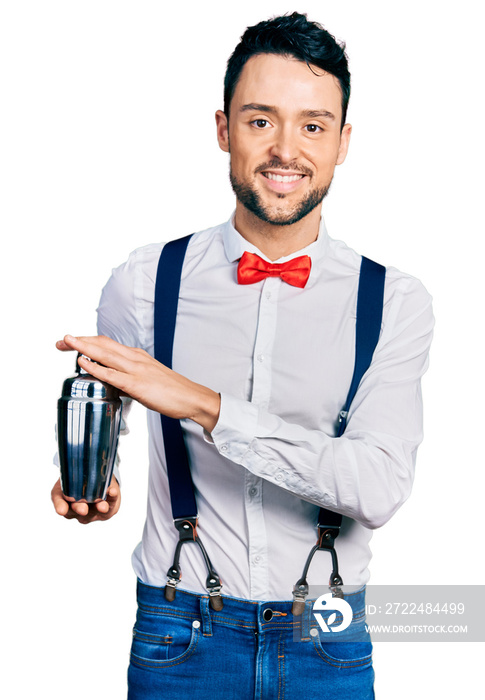 Hispanic man with beard preparing cocktail mixing drink with shaker smiling with a happy and cool smile on face. showing teeth.