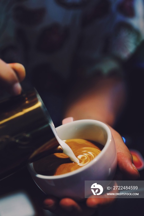 Close up barista hands making coffee latte art over dark background.