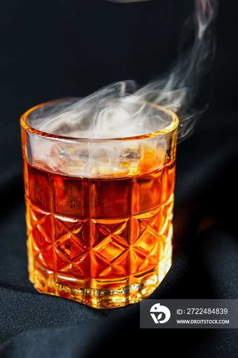 Alcoholic drink. A cocktail with whiskey or cognac with fire and smoke close-up, dark black background. Concept of elite alcohol and nightlife