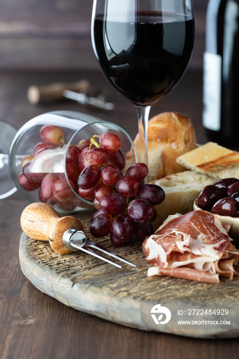 Rustic charcuterie board with red wine and grapes against a wooden background.