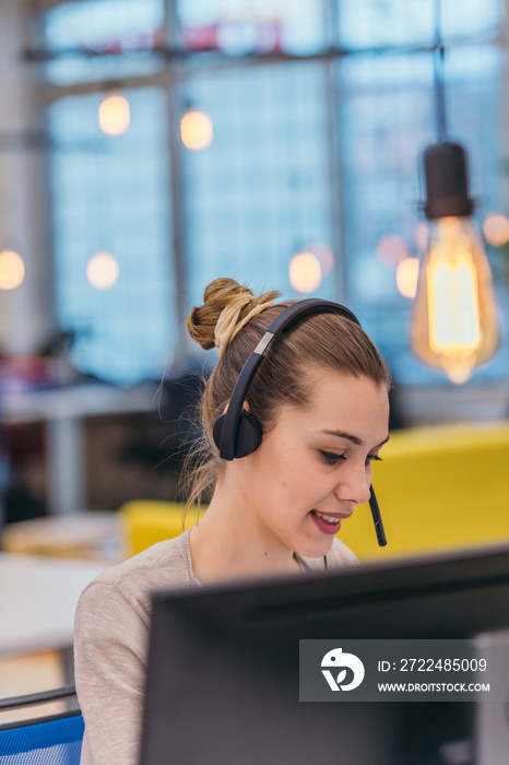 Pretty female customer representative  working on her laptop while speaking with her client on her headset