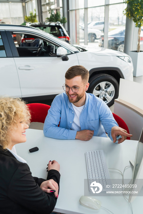 Car dealership manager with client at computer in showroom