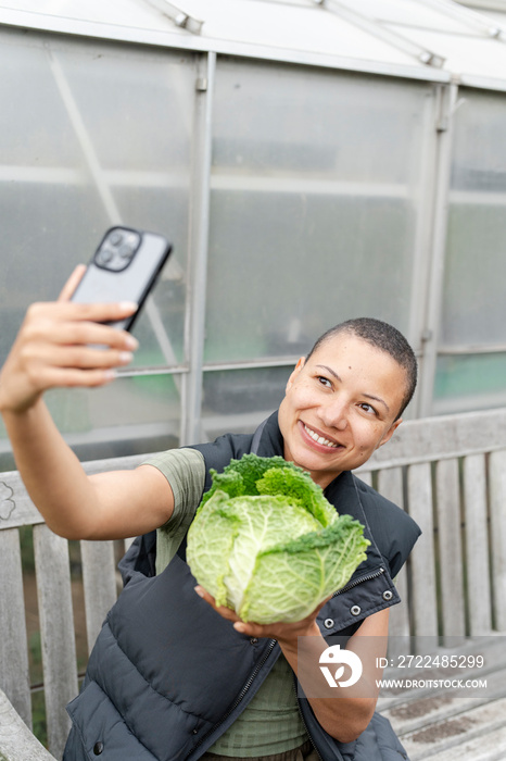 Smiling woman taking selfie with homegrown cabbage in allotment