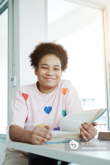 Smiling African student or pupil girl is reading a book in library at school. She is enjoy for learning at home for homeschool. Education and teenage Concept.