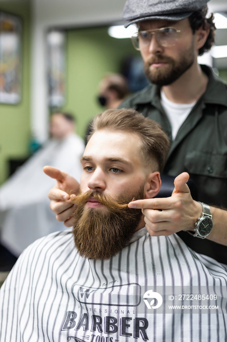 Getting perfect shape. Close-up side view of young bearded man getting beard haircut by hairdresser at barbershop