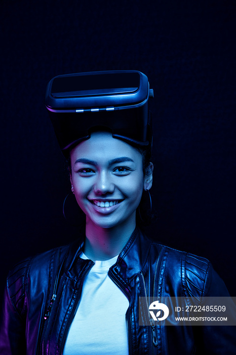 African-American smiling girl in vr glasses with a virtual reality headset isolated on a black background, illuminated by neon lights