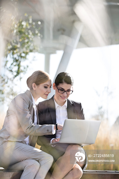 Happy businesswomen using laptop together on sunny day