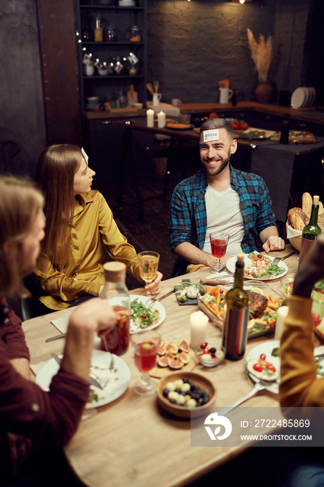 High angle view at group of friends playing guessing game while enjoying dinner party sitting at table in dark room, copy space