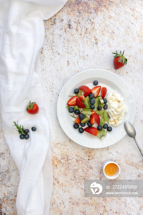 A plate of fruit and yoghurt with honey, strawberry, kiwi, blueberry shot from above, flatlay and space for text