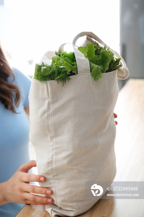 Young woman with fresh vegetables in eco bag indoors