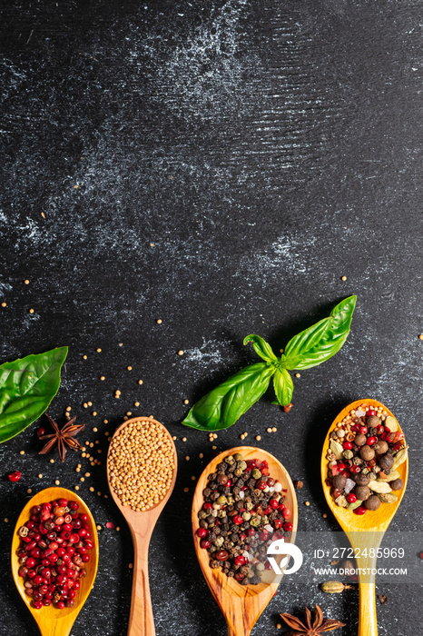 Wooden spoons with different aromatic organic spices on black wooden table with copy space for your text. Recipe book cover concept. Restaurant menu template.