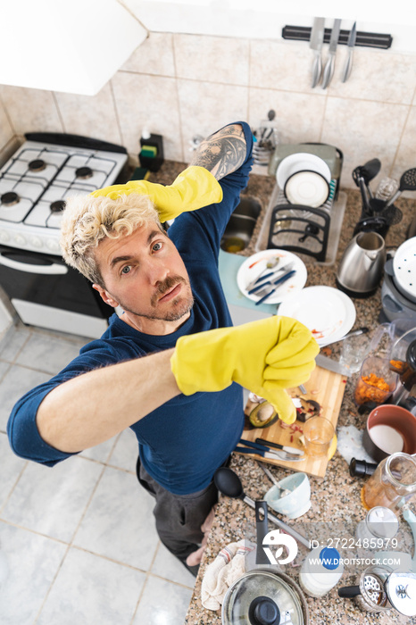 Top view of man wearing cleaning gloves with thumbs down because of his messy kitchen