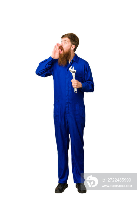 Young adult redhead mechanic man full body isolated shouting and holding palm near opened mouth.