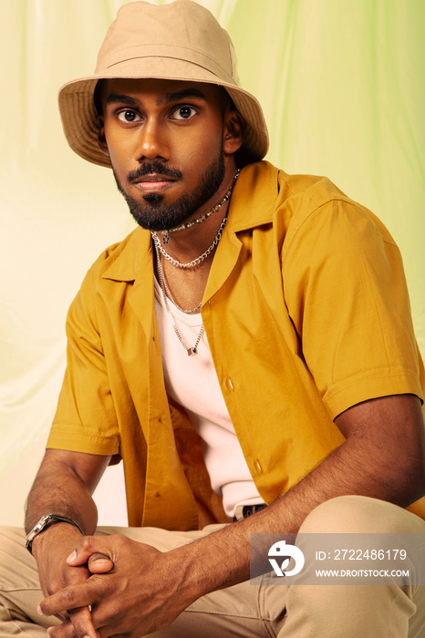 Malaysian Indian man posed in front of a cloth background, styled in a yellow shirt and hat