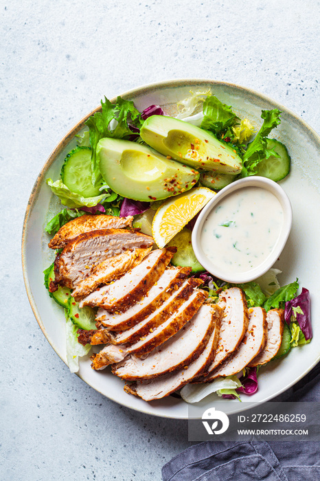 Grilled chicken salad with avocado, cucumber and dressing, top view. Healthy food concept.