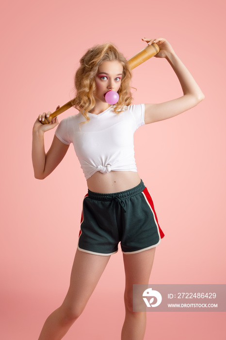 Beautiful young girl with bright makeup and hairdo in retro 90s fashion style in image of Harley Quinn isolated over pink studio background. Concept of eras comparison