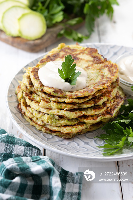 Zucchini fritters with yogurt sauce on white wooden table