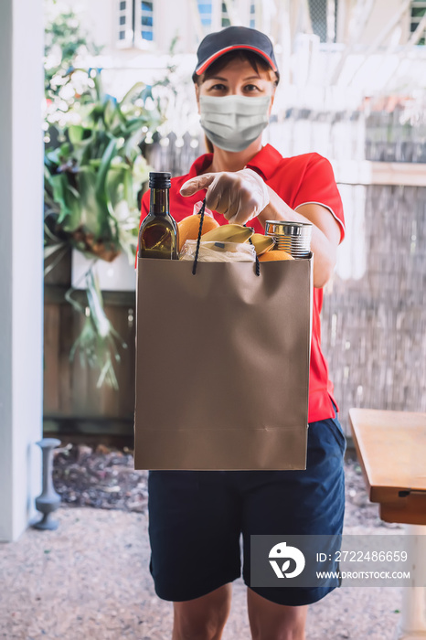 Delivery woman in protective face mask and gloves delivers paper bag with food products. Health protection, safety and pandemic concept.