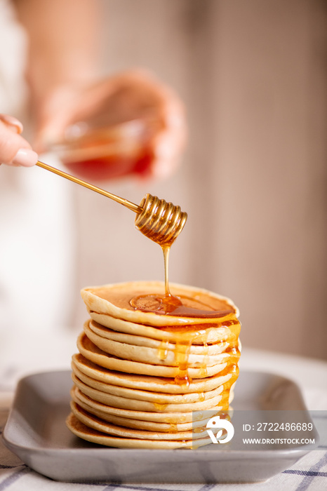 Hand of young housewife dripping fresh honey from dipper on top of pancake