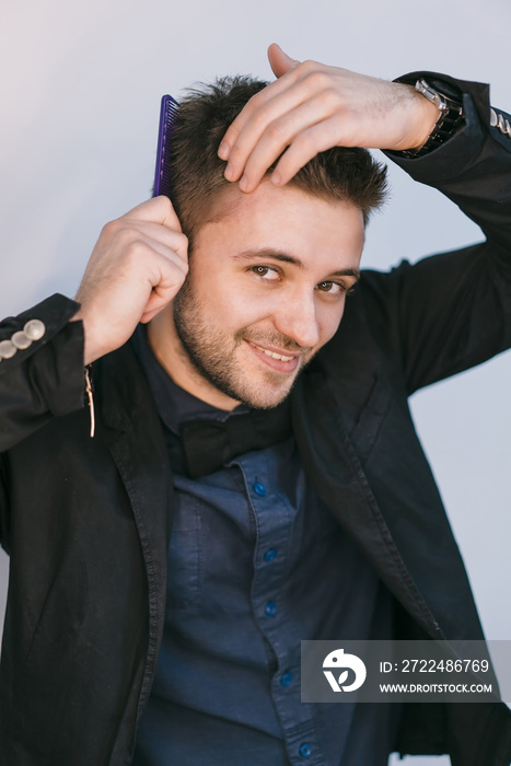 a smiling man in a black jacket combs his hair with a comb in the studio. Close-up