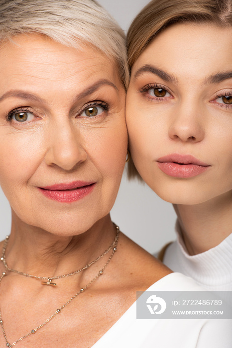 close up of young woman and mature mother looking at camera isolated on grey