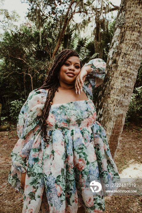 plus size Black woman wearing dress leans against tree