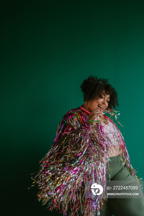 portrait of a plus size person wearing a rainbow tinsel jacket dancing