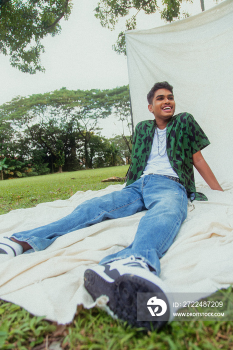 Malaysian Indian men in a group against a cloth backdrop in a park surrounded by trees, talking, laughing and sitting together