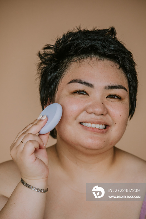 closeup portrait of a plus size filipino woman applying sponge to skin